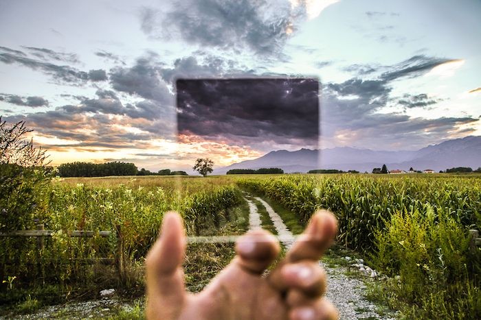 Picture : Hand holding a piece of glass in front of a field.